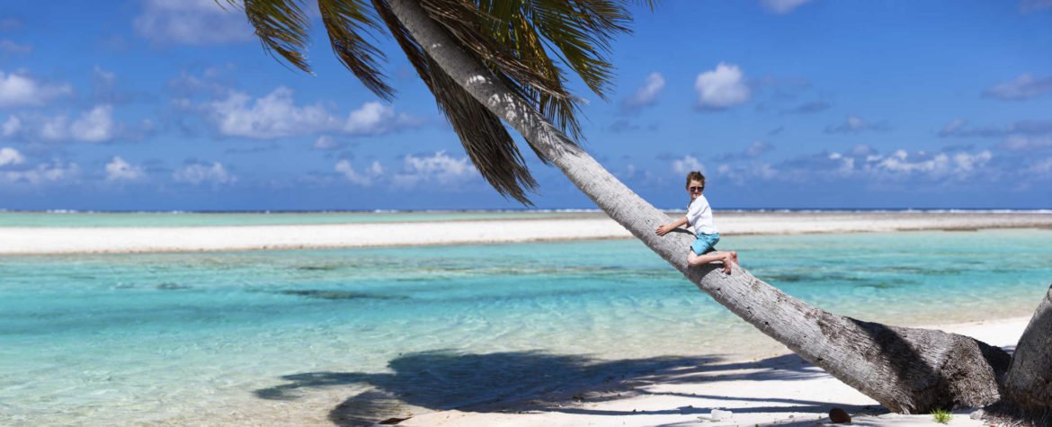 little boy on palm tree on white sand beach with turquoise water in French Polynesia
