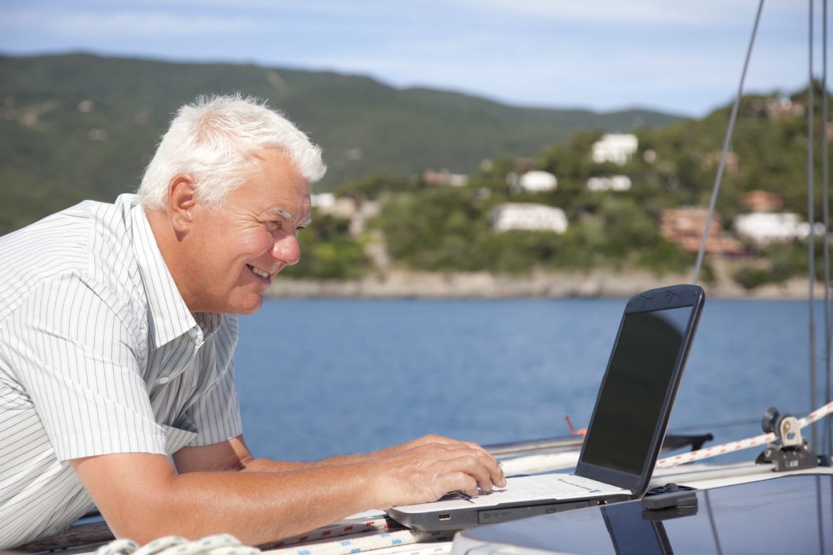older white male looks at laptop on charter yacht